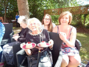 Resident and relatives in the garden, smiling to the camera with their scones
