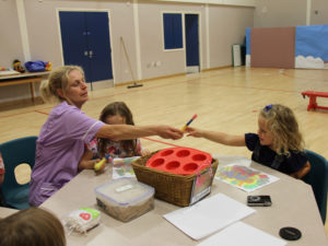 Care Assistant, Caroline, passing the paint brush to one of the children