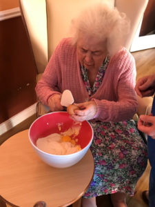 Cedar Lodge resident cracking egg into cake mix