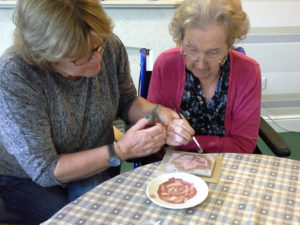 Mary Kembery supporting resident painting clay leaf tiles