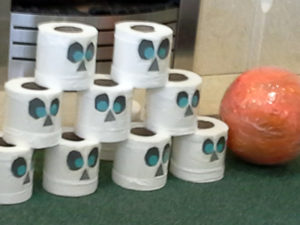 Halloween bowling with a ball and toilet paper with drawn on spooky faces